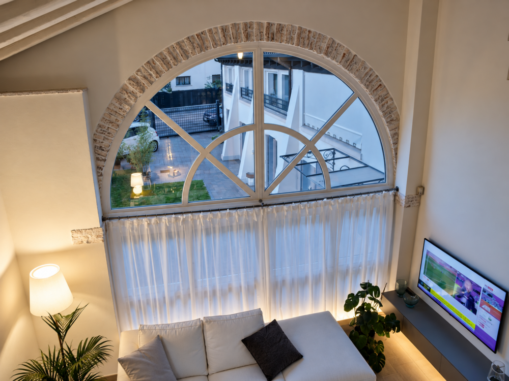 Finestra ad arco sul soggiorno con tende e vista sulla corte